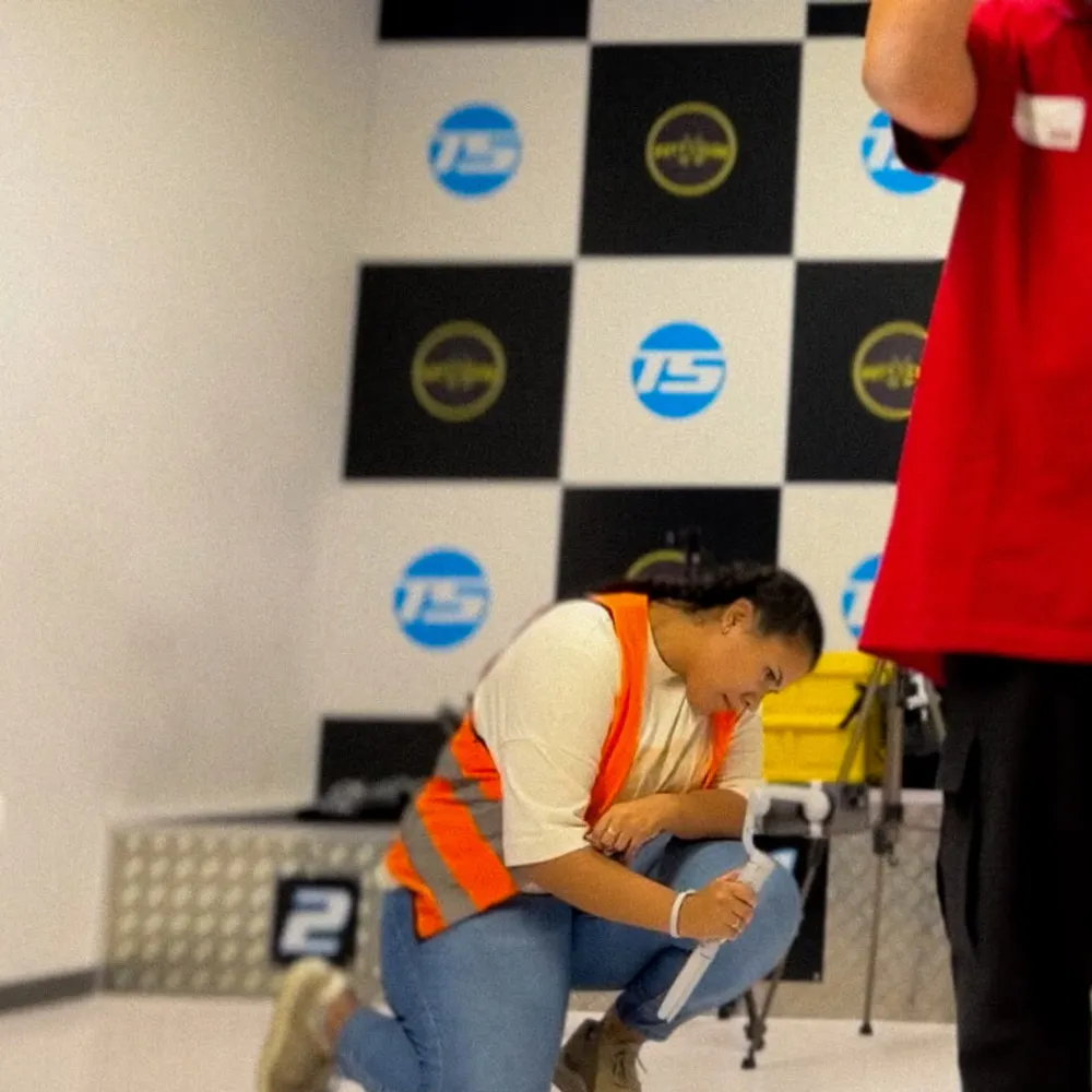 A female track marshal kneeling and laughing in front of the checkered flag wall