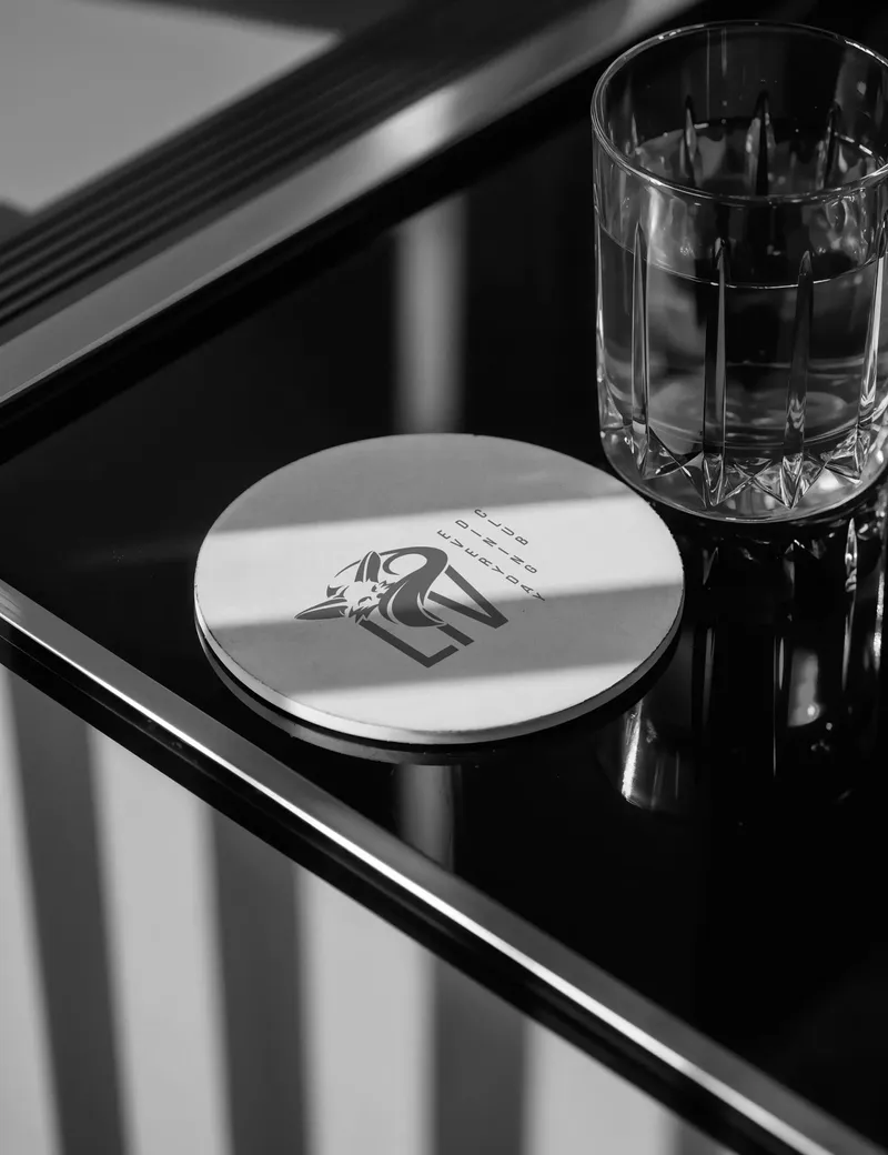 Round coaster with the Liv mark next to a glass of water on a dark counter