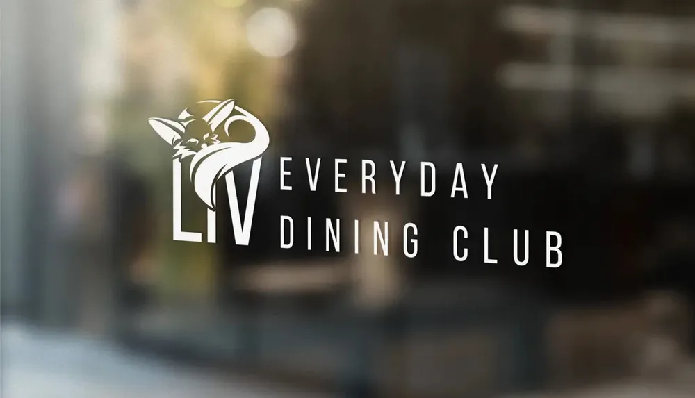 The Liv logo as white vinyl on a window pane, with the dining room blurred behind it
